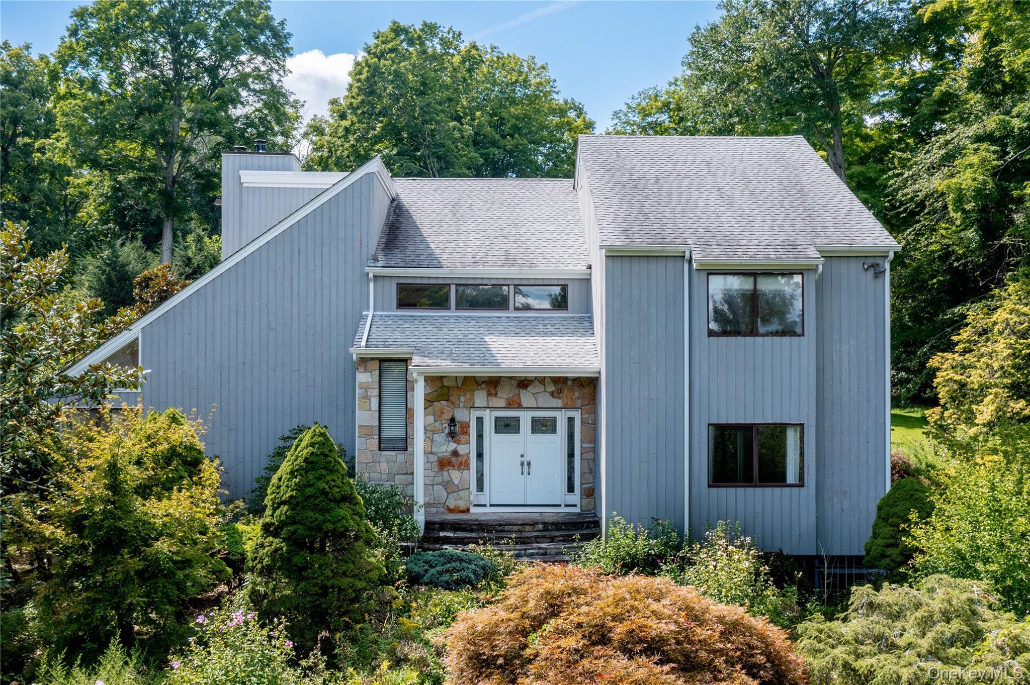 Contemporary exterior featuring vertical siding, a stone facade entry, a gabled roofline, and ample natural landscaping