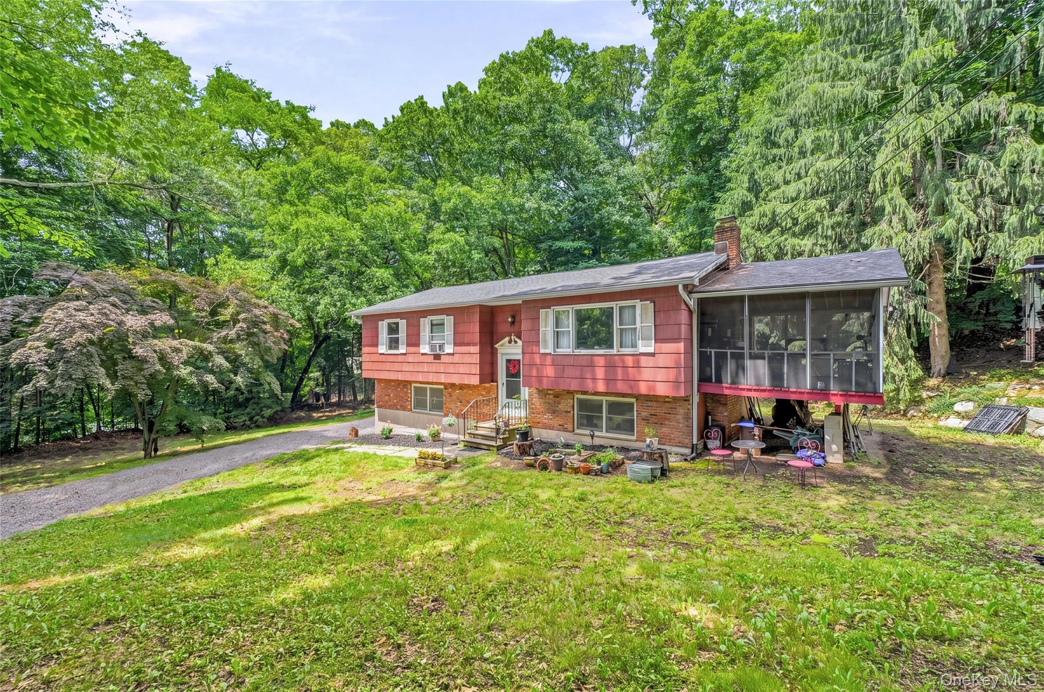 Raised ranch house featuring a red siding and brick facade, a screened-in porch, a paved driveway, and mature landscaping