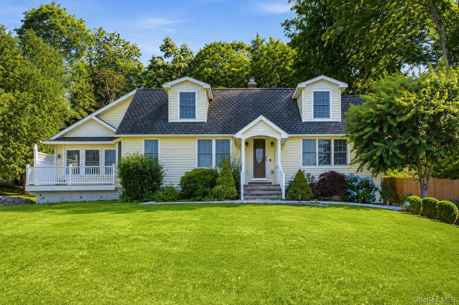 Exterior featuring light yellow siding, a prominent dormer window, and a covered front entry with white railings