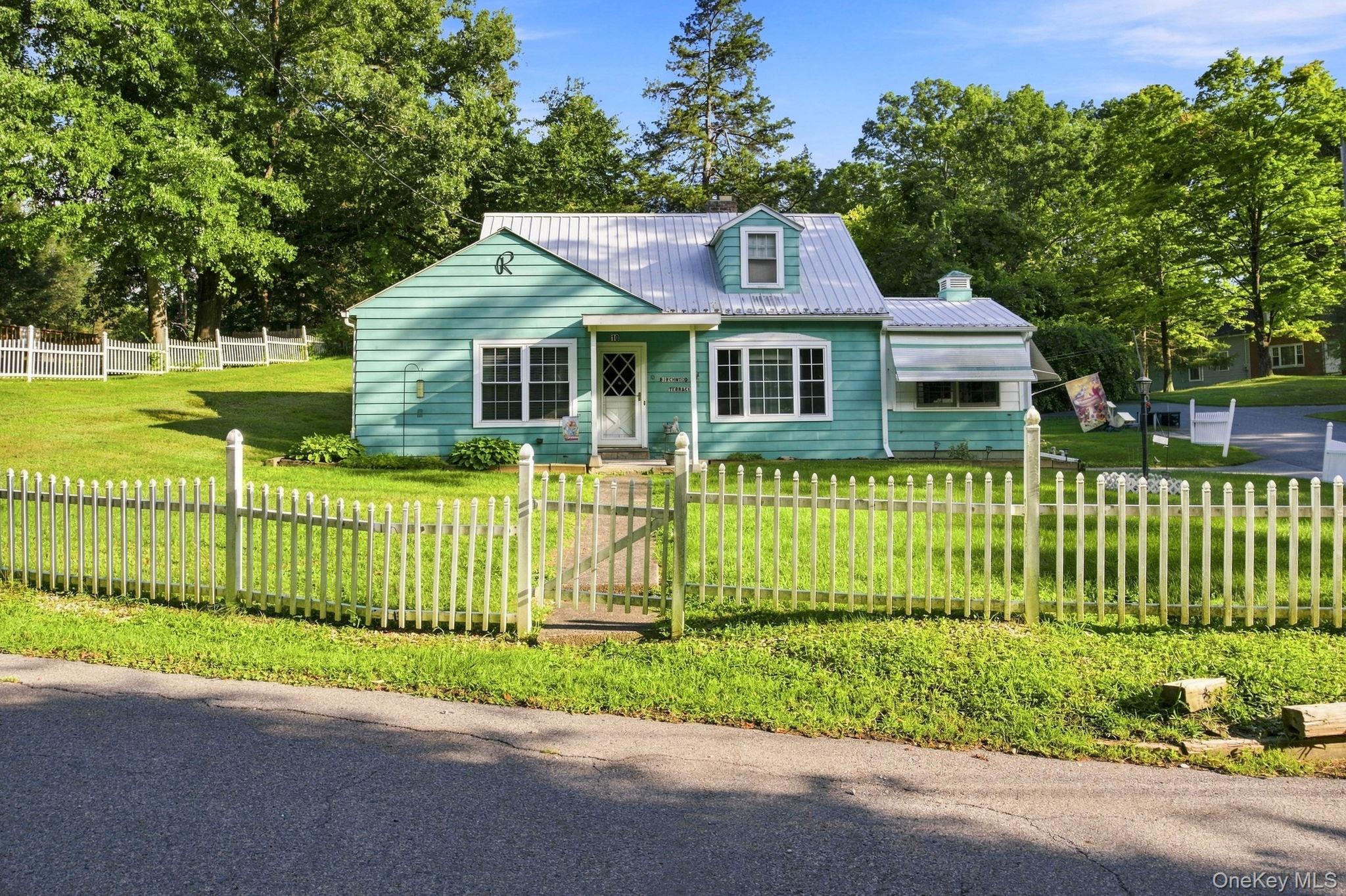 Turquoise siding with white trim and a white picket fence, and metal roof.