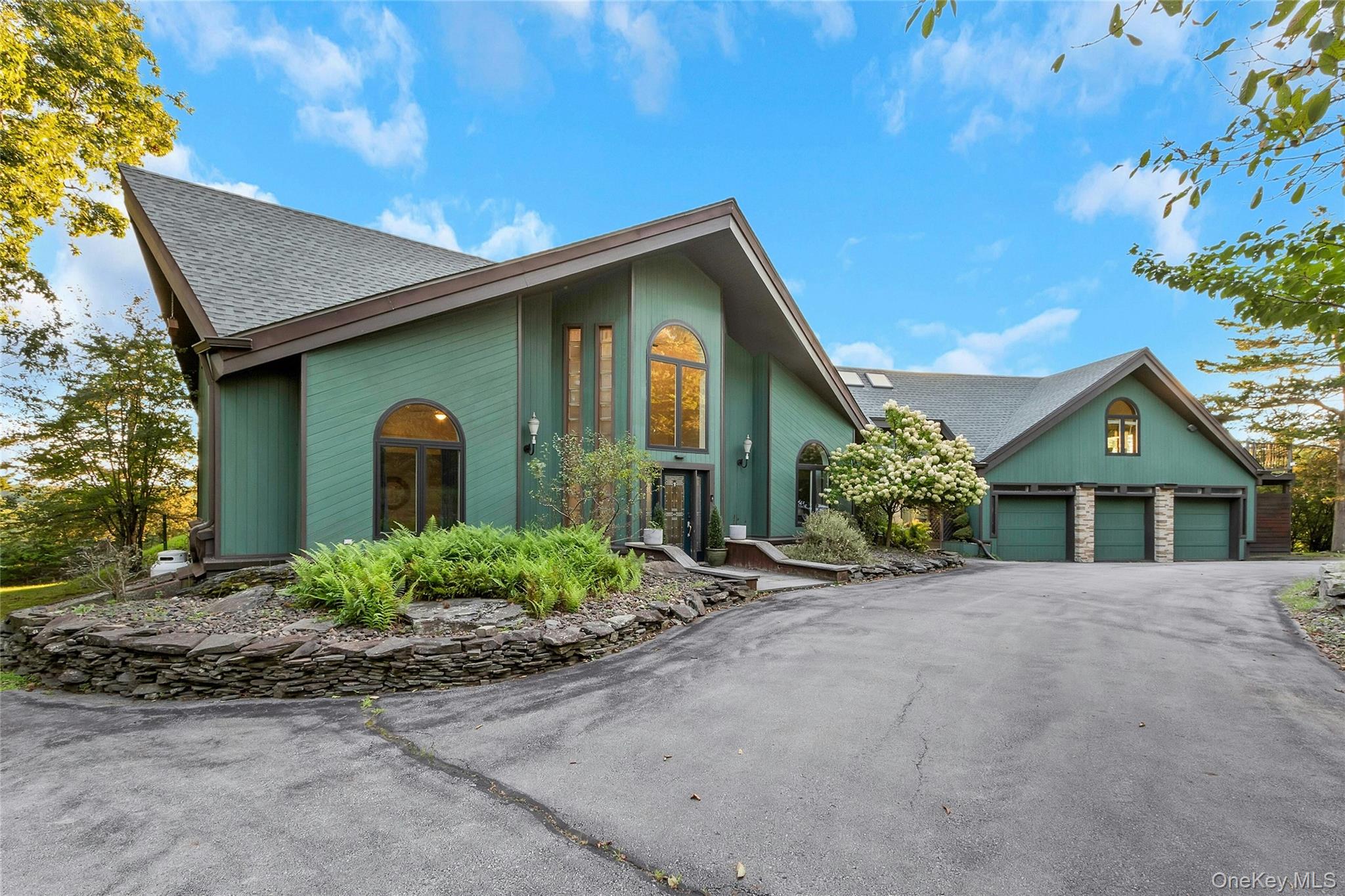 Contemporary exterior with a multi-level roofline, extensive driveway, attached three-car garage, and established landscaping