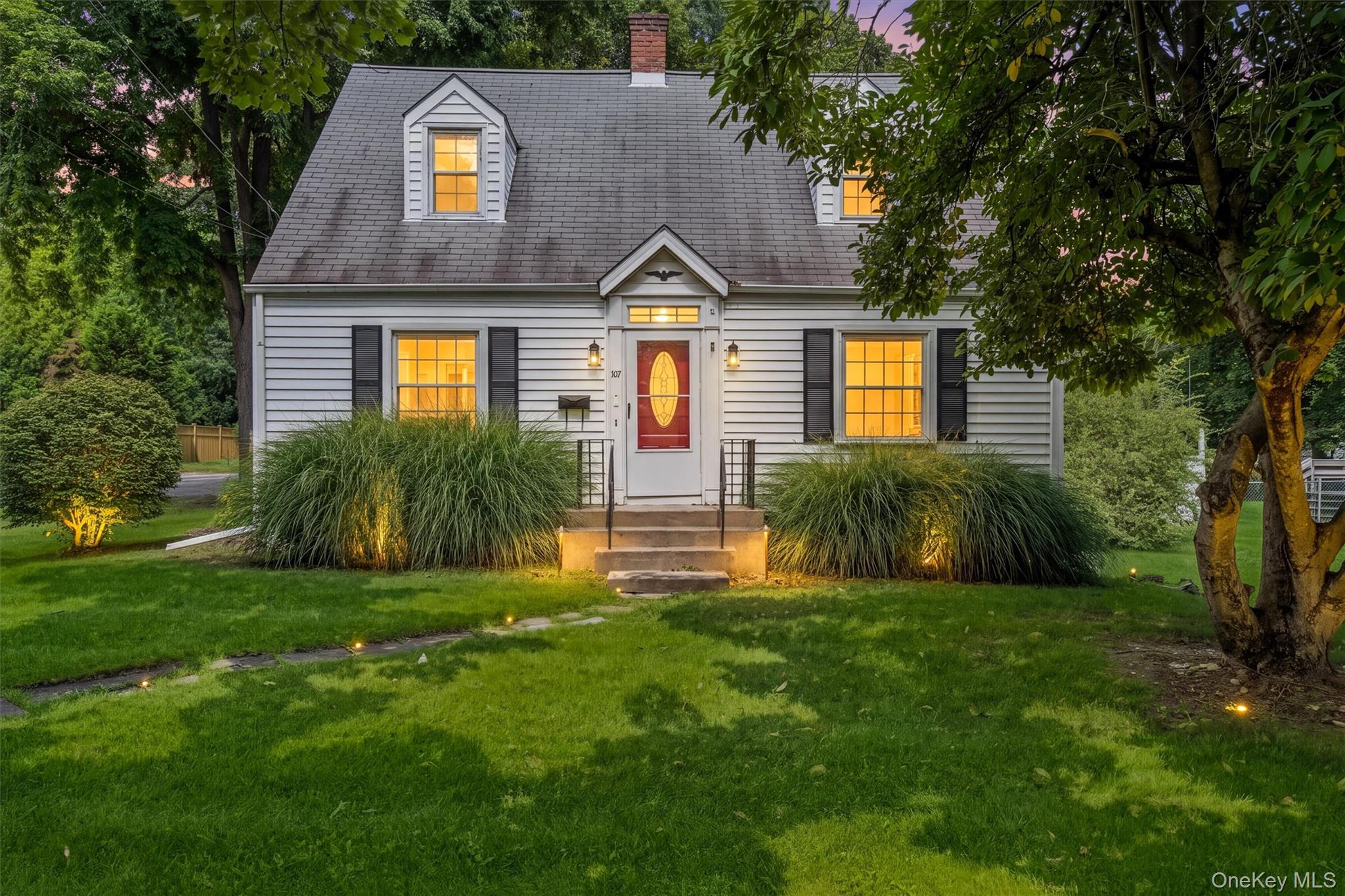 White siding exterior with black shutters, dormer windows, red entry door, and a gray shingled roof
