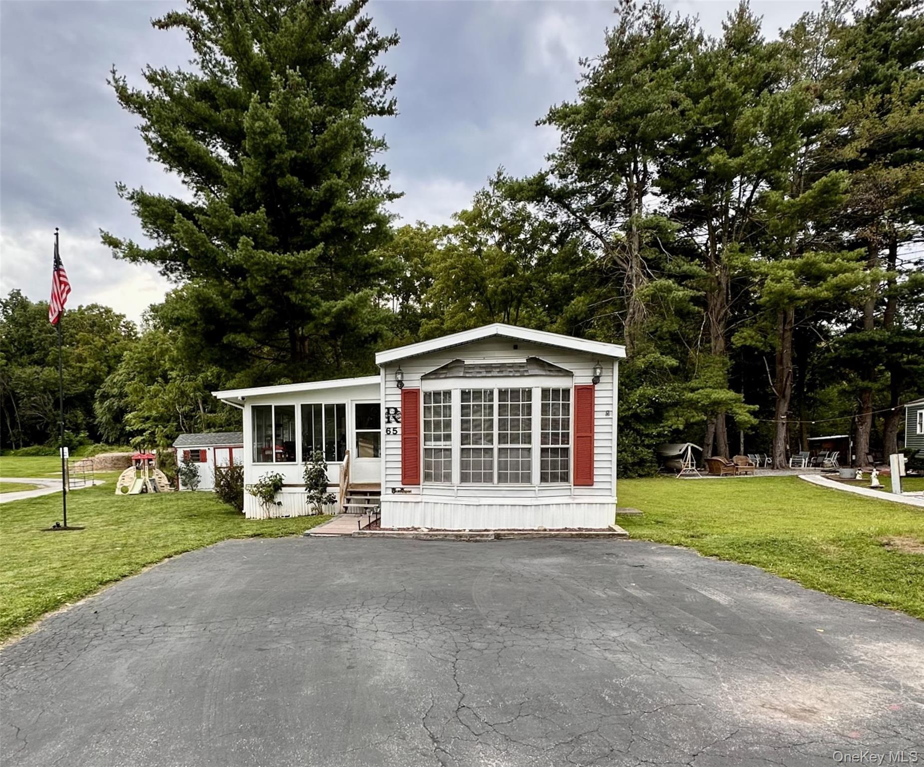 White siding exterior featuring a sunroom, bay window with red shutters, and an asphalt driveway.