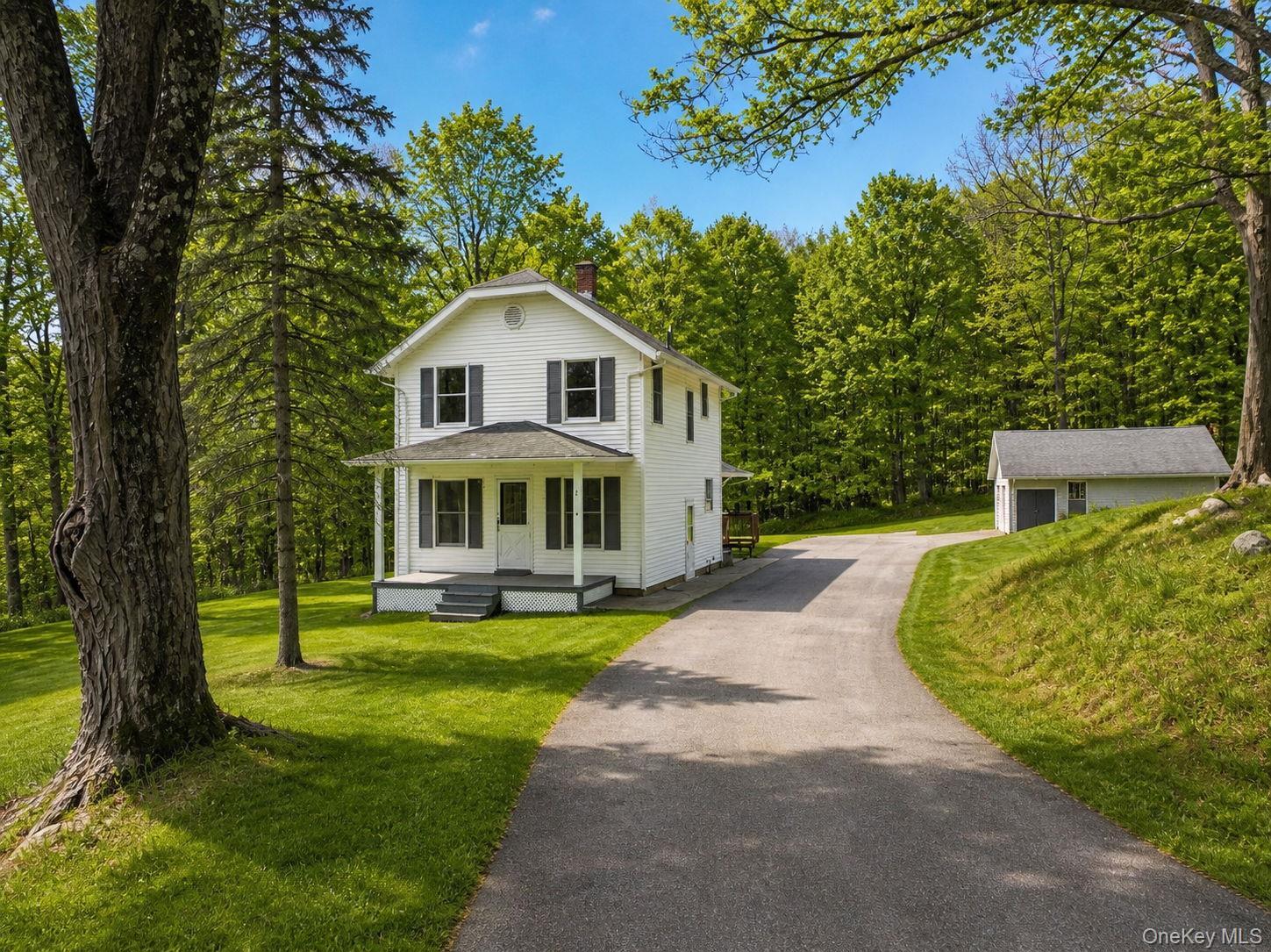 Two-story white residence featuring a covered front porch, black window shutters, and a grey asphalt driveway