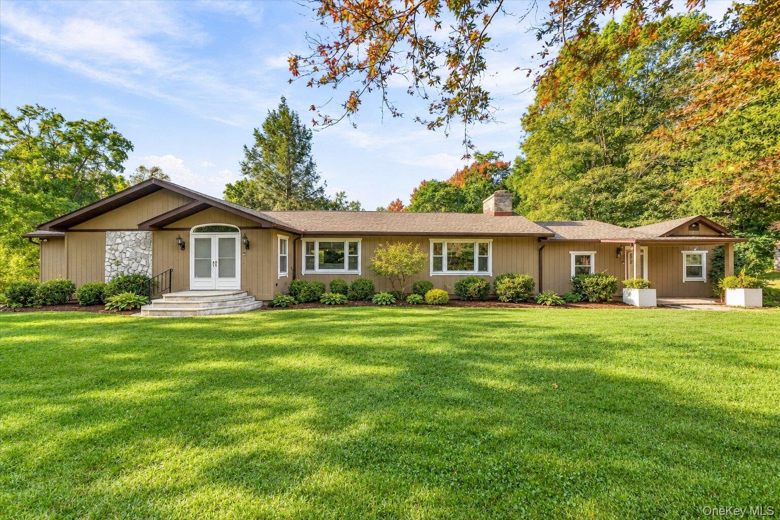 Virtually Staged. Welcoming front exterior with mature landscaping, a spacious lawn, and a distinctive stone-accented entry.