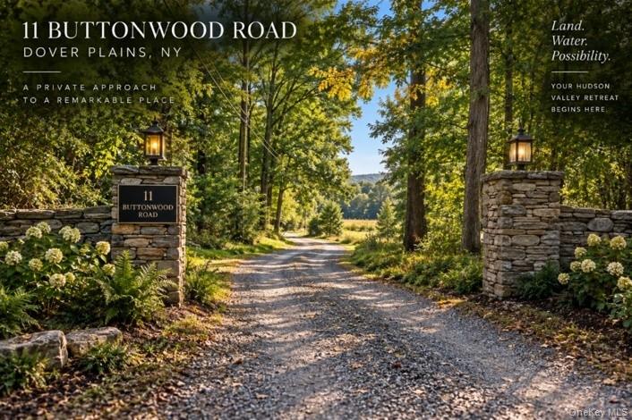 Digitally Imagined.Gravel driveway entrance framed by stacked stone pillars, featuring integrated lanterns, lush landscaping, and a distant tree-lined horizon