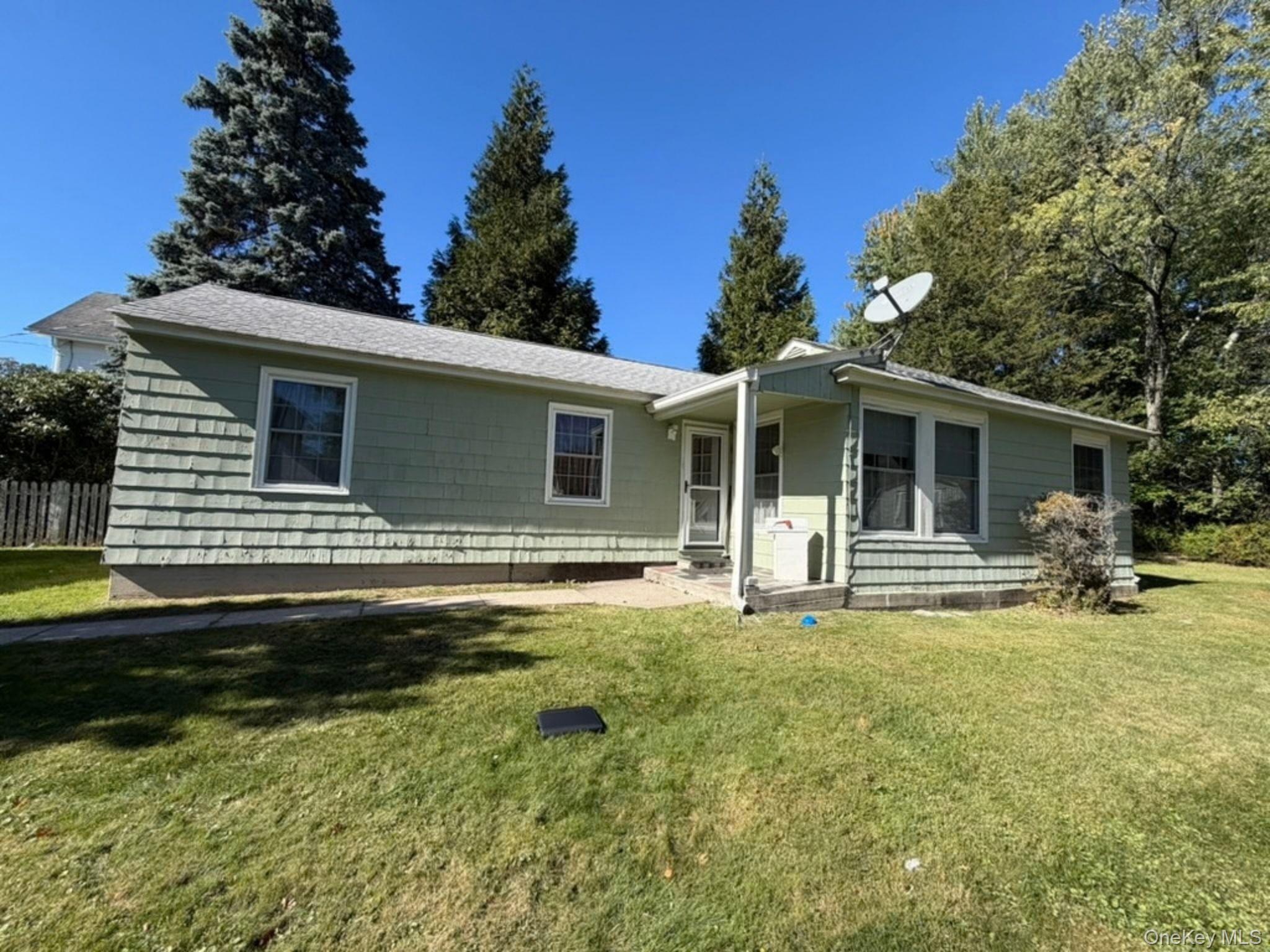 Light green shingle siding, multiple windows, and a paved walkway