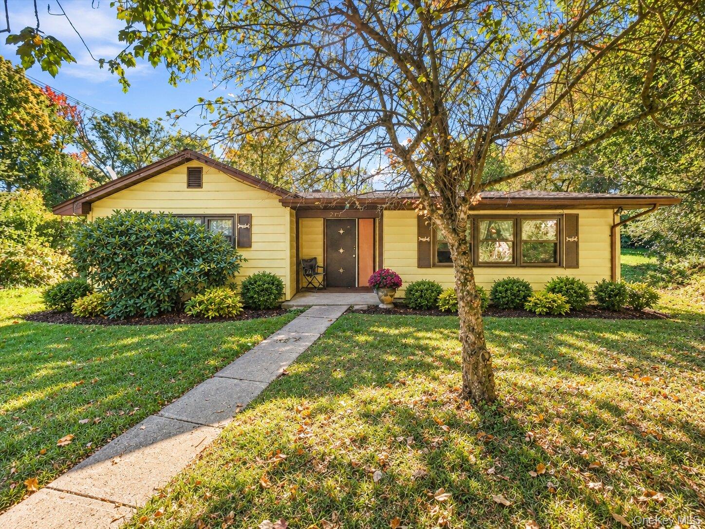 Virtually decluttered. Front exterior view of the single-story home featuring a covered entry, mature trees, walkway, and established landscaping.