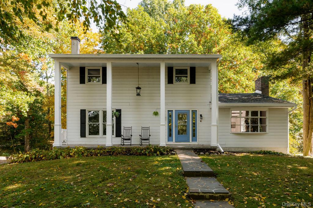 Two-story residence featuring a covered front porch with square columns, light-colored horizontal siding, dark window shutters, and a natural stone walkway
