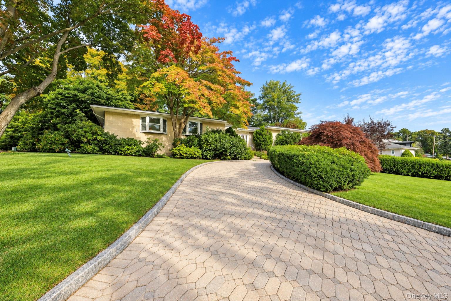 Brick exterior featuring a paved stone driveway, manicured landscaping, mature trees, and bay windows