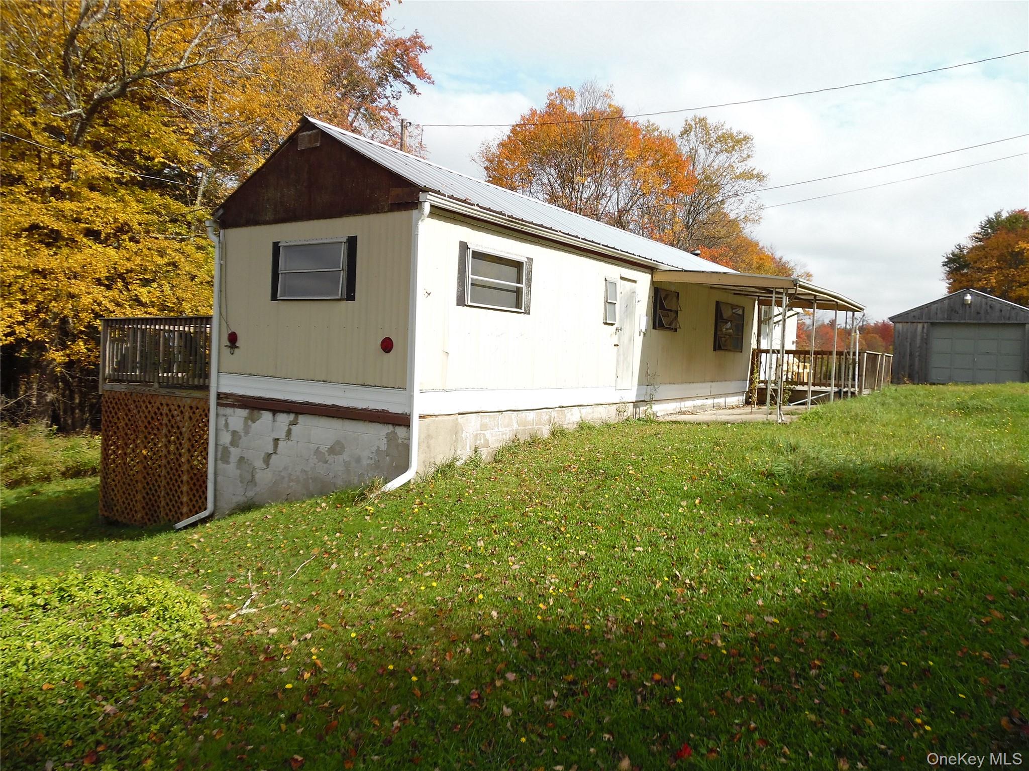 Exterior featuring light-toned siding, a metal roof, a wood-framed deck with lattice skirting, a covered porch, and an attached garage