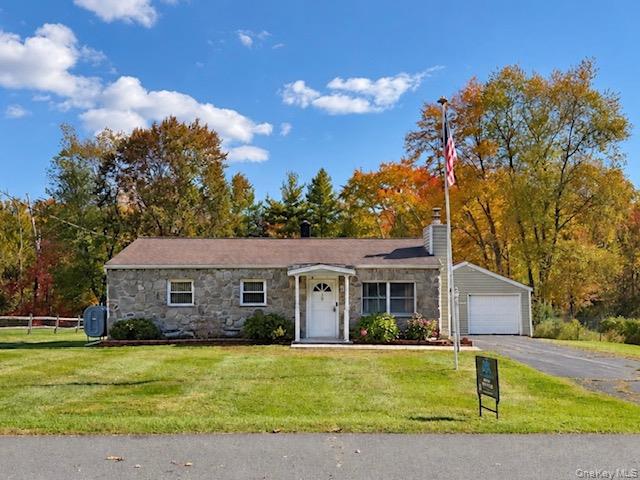 Single-story stone facade exterior featuring a covered front entryway, asphalt shingle roof, attached garage, paved driveway and flag post