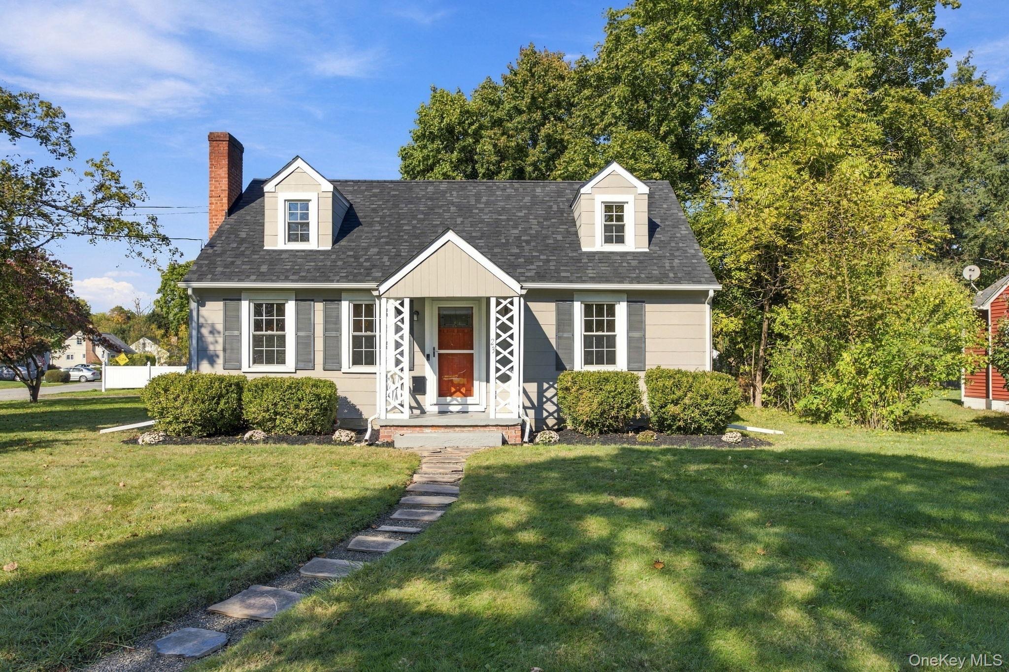 Cape Cod style exterior featuring a covered entryway with lattice detailing, dual roof dormers, a masonry chimney, and a stone paver walkway