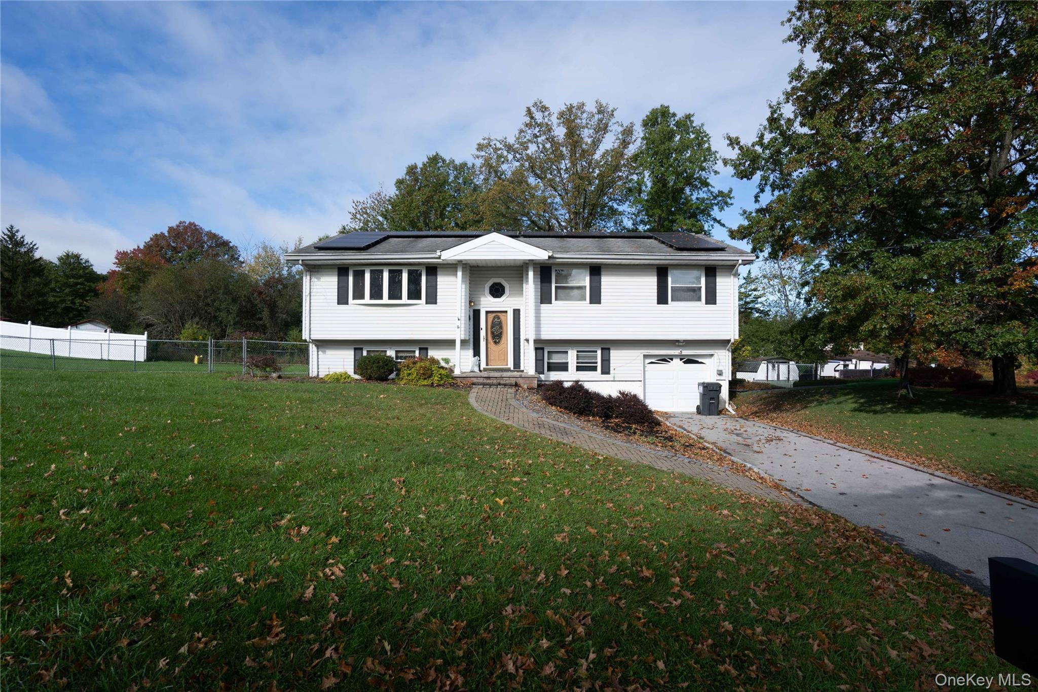 Split-level exterior featuring white siding, a paved driveway, attached garage, integrated solar panels, and a front entryway with a decorative window detail